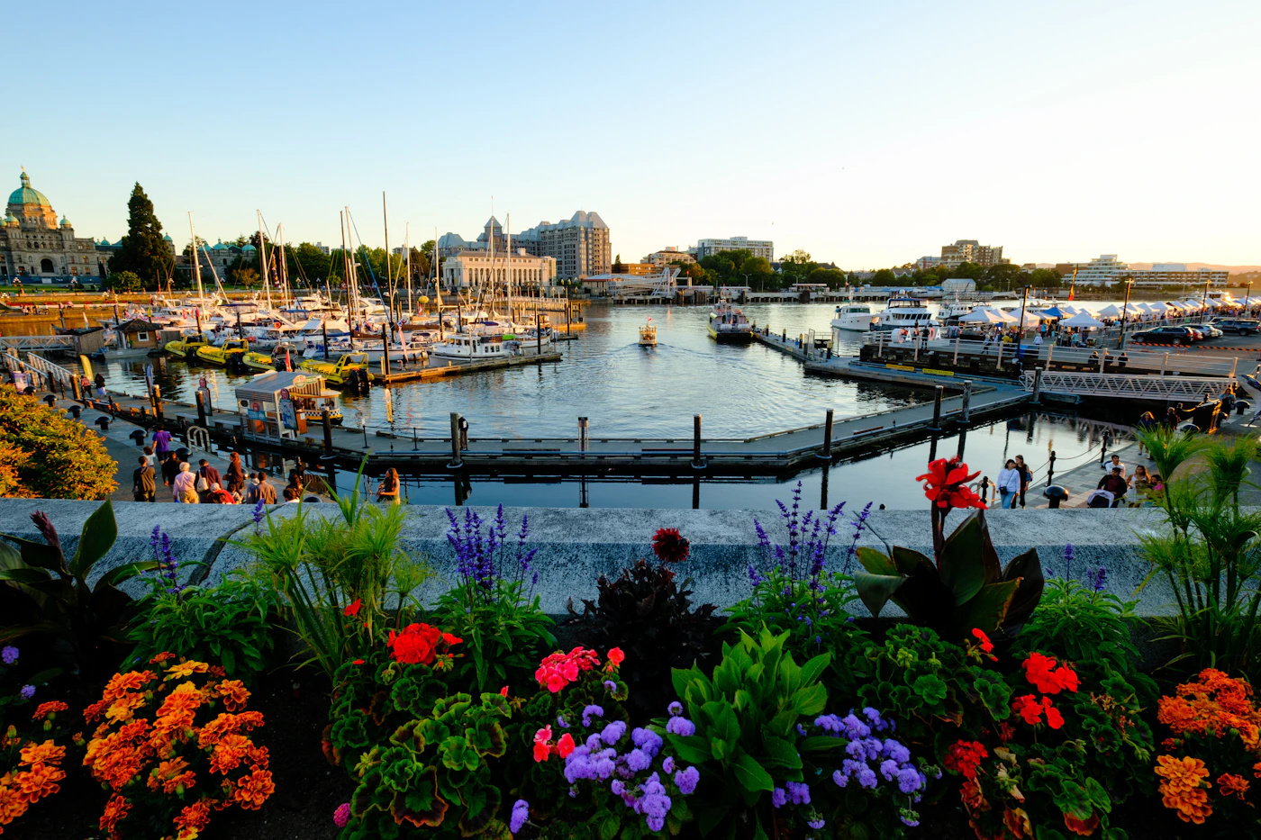 Colourful flowers above Victoria’s Inner Harbour, with boats and people along the waterfront.